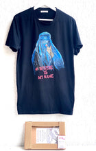 Full view of a black t-shirt hand-painted with a portrait of a veiled Afghan woman in a blue burqa, revealing red nails and red lipstick, with #whereismyname.