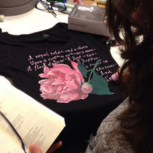 Side and back view of artist painting a personalized rose design with Emily Dickinson poem on a T-shirt – surrounded by brushes, paints, and books