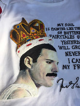 Close-up of hand-painted Freddie Mercury profile with crown and butterfly on black fabric, featuring poetic phrase.