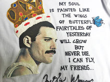 Close-up of hand-painted Freddie Mercury profile with crown and butterfly on black fabric, featuring poetic phrase.