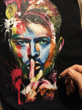 Close-up of artist’s hands painting David Bowie’s colorful portrait on a black T-shirt – intense 3D texture