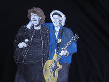 Close-up of Mick Jagger & Keith Richards hand-painted on a t-shirt with his arm resting on Mick Jagger’s shoulder, wearing an electric blue shirt and holding a guitar.