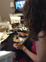 Side view of artist seated at table painting a personalized T-shirt – surrounded by brushes and fabric paints

