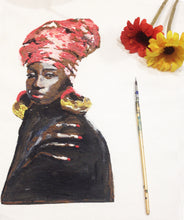 Partially visible white T-shirt on table featuring a painted Black Queen portrait – brush resting beside the artwork