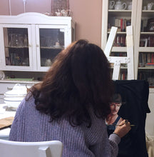 Back view of artist painting a custom T-shirt on an easel – table with brushes and fabric paints visible

